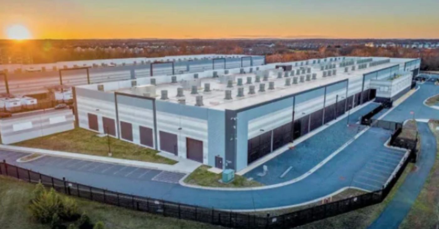 Aerial view of a large modern warehouse facility at sunset, with loading bays along the side and a curved driveway nearby.